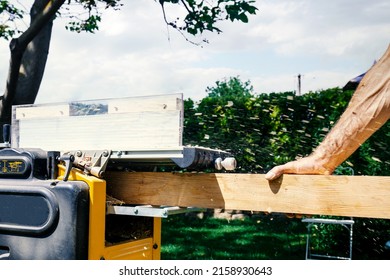 Joiner, Man's hand scouring a wooden board on a thickness machine in garden. Carpenter working with electric planer on wooden beam, plank. DIY concept