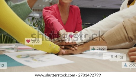 Joining colleagues placing hands in stack in meeting room with bright sleeves, charts and reactions. Teamwork, collaboration, office, openplan, graphs, engagement, modern