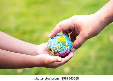 Joining forces to take care of global. Blurred green lawn background. Protect our globe. A mother's hands pass on a small world to her baby's little hands. To help protect and keep our planet livable.