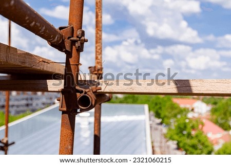 Joint of steel rusty scaffolding with tread, wooden plank for trampling placed on construction site.