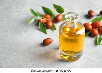 Jojoba oil in glass bottle and seeds on light grey table