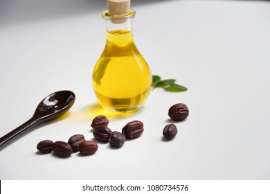 Jojoba seeds and oil in a transparent glass bottle and green leaves