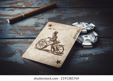 A Joker Card With Cigarette And Poker Chips On The Old Wooden Background, Close Up Shot. Russia, Saint-Petersburg, August 2022. High Quality Photo.