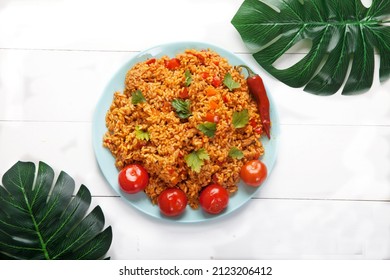 Jollof Rice With Tomatoes And Hot Peppers On A Blue Plate On A White Plate With Monstera Palm Leaves. National Cuisine Of Africa.