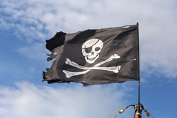 Jolly Roger Pirate Flag On Blue Sky Background.