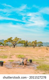 Jos East, Plateau State - May 12, 2021: Young African NGO Representative Visiting Rural Communities For Clean Water Projects On A Sunny, Bright And Blue Landscape Standing By A Well