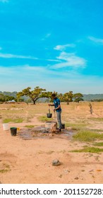 Jos East, Plateau State - May 12, 2021: Young African NGO Representative Visiting Rural Communities For Clean Water Projects On A Sunny, Bright And Blue Landscape Standing By A Well