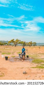 Jos East, Plateau State - May 12, 2021: Young African NGO Representative Visiting Rural Communities For Clean Water Projects On A Sunny, Bright And Blue Landscape Standing By A Well