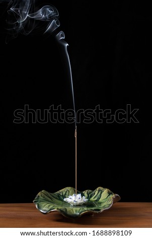 a joss stick burning on a lotus shape holder in front of black background