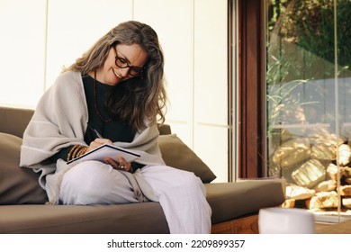 Journaling During Retirement. Mature Woman Smiling Happily While Writing In Her Journal At Home. Cheerful Senior Woman Writing Down Her Thoughts While Sitting On A Couch.