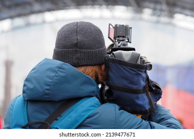 Journalist With A Camera In Winter, Back View. Cameraman Using Professional Camcorder In The Street