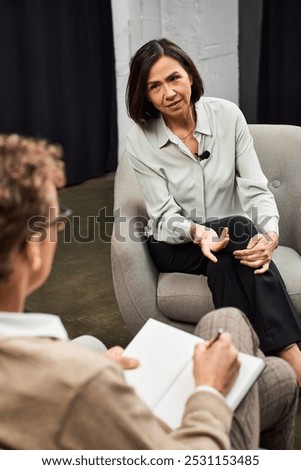 A journalist conducts a focused interview with a knowledgeable woman in a professional environment.