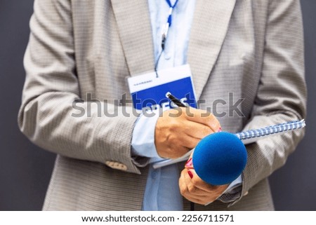 Journalist correspondent or reporter with press pass at media event, holding microphone, writing notes. Journalism concept.