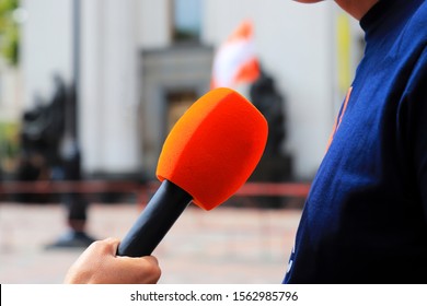 The Journalist Holds A Red Microphone In His Hand And Interview On The Street. Television Reporter With Microphone At A Mass Event, Press Conference, Business.