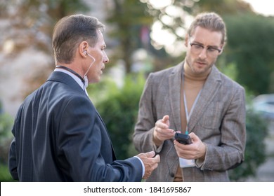 Journalist Job. Fair-haired Male Journalist Helping His Collegue Fit Headset