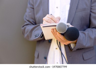 Journalist at media event or news conference, holding microphone, writing notes. Broadcast journalism concept.