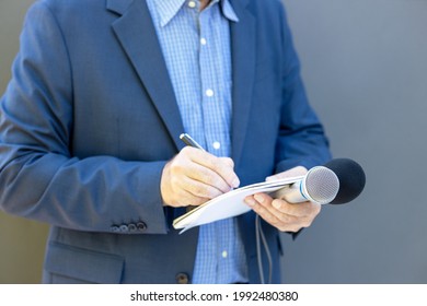 Journalist at news conference or media event, holding microphone, writing notes. Broadcast journalism concept.
