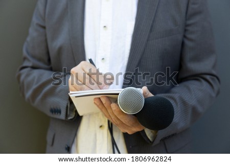Journalist at news conference or media event, writing notes, holding microphone