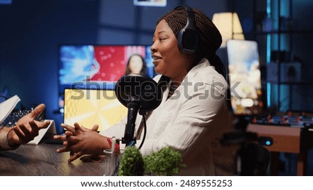 Journalist records interview with cellphone on tripod stabilizer in studio, reviewing notes to ask quality questions to guest. Close up of woman using phone to film vlog, talking on mic with celebrity