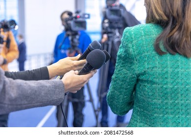 Journalists at news conference holding microphones making media interview with female politician or business woman