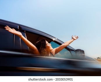 Journey of happy Asian woman with short hair hands up with blur motion from black car movement on blue sky background. Female travelers enjoy and smiling while looking at the view, on sunny days.