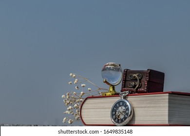 Journey And Learning Concept Background. Crystal Globe, Pocket Watch And Stack Of Books With A Sky Background. Copy Space.