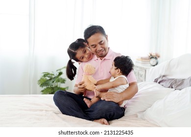 The Joy Of An Asian Single Father Taking Care Of Two Children, A Daughter And A Son. A 2-year-old Is Sitting On His Father's Lap And Playing Happily In Bed. Concept Happy Family