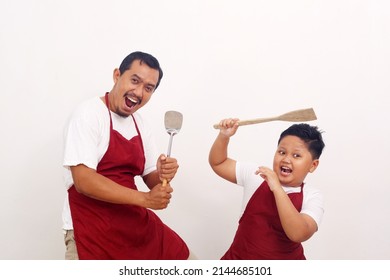 The joy of a father and son wearing kitchen apron while holding kitchen ware. Isolated on white
