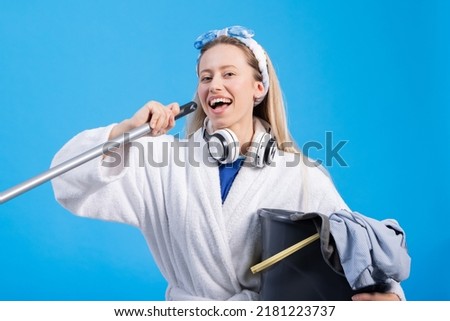 Joy laughs while cleaning. Cheerful woman holds bucket and mop fooling around, dancing positive mood in the house. Portrait on blue background.