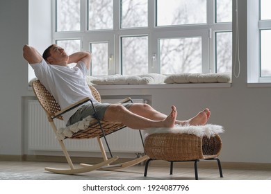 Joy of life. Total relaxation. Handsome young man keeping eyes closed and holding hands behind head while sitting in big comfortable chair at home