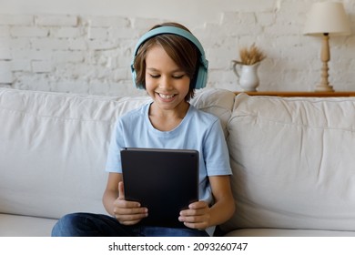 Joyful 12s preteen kid boy in wireless headphones using digital computer tablet, watching entertaining or educational video online, communicating in social network, holding webcam call, playing games. - Powered by Shutterstock