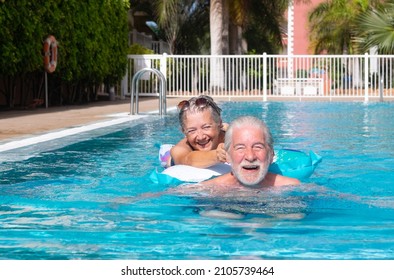 Joyful 70s mature adult active happy senior couple of grandparents having fun in the swimming pool floating on mattress outdoors in water. Relaxed retired people enjoying vacation healthy lifestyle