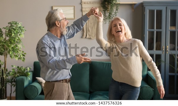 居間で笑いながら踊る楽しい活動的な老夫婦 家で楽しい中年の妻と年上の夫 笑顔で仲良く過ごす祖父母 の写真素材 今すぐ編集
