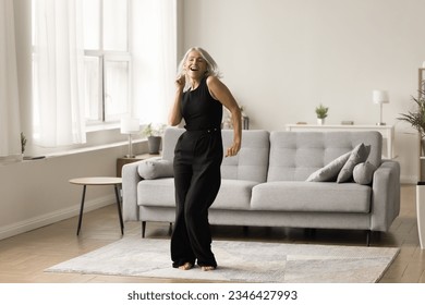 Joyful active senior lady excited with single dance at home enjoying motion, activity, music, singing song, having fun in cozy comfortable living room interior. Full length wide shot - Powered by Shutterstock