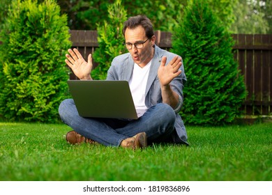 Joyful Adult Businessman Sits On Grass Works Outdoors, Looks With Surprise At Laptop Screen, Man Happy With Stock Growth And Higher Earnings Profit, Profitable Proposition, Winner, Success Concept