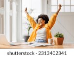 Joyful african american business woman freelancer   smiling and rejoices in victory while sitting at desk   and working at laptop screen after finishing project  in home office
