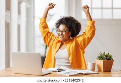 Joyful african american business woman freelancer   smiling and rejoices in victory while sitting at desk   and working at laptop screen after finishing project  in home office
 - Powered by Shutterstock