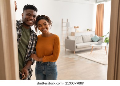 Joyful African American Family Couple Embracing Standing In Opened Doors Of Their New Home, Smiling Looking At Camera. Housing For Married Couple. Real Estate Property Ownership Concept