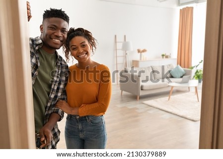 Joyful African American Family Couple Embracing Standing In Opened Doors Of Their New Home, Smiling Looking At Camera. Housing For Married Couple. Real Estate Property Ownership Concept