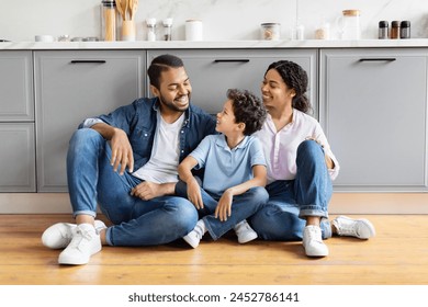 A joyful African American family sharing a laugh while sitting on a modern kitchen floor, representing familial bliss - Powered by Shutterstock