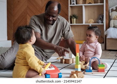 Joyful African American father sitting on floor in living room at home playing with his cute twin babies showing them toy tower - Powered by Shutterstock