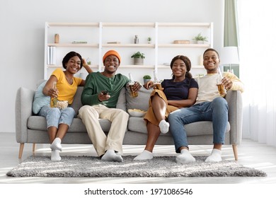 Joyful African American Friends Sitting On Sofa, Watching TV And Drinking Beer At Home, Copy Space. Happy Group Of Young Black Men And Women Enjoying Time Together, Having Party