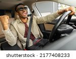 A joyful african american in glasses dances in a car, sings while driving his car. Road fun