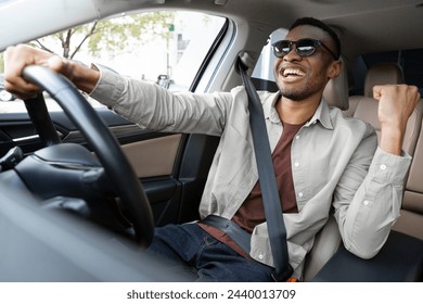 A joyful african american in glasses dances in a car, sings while driving his car. Road fun - Powered by Shutterstock