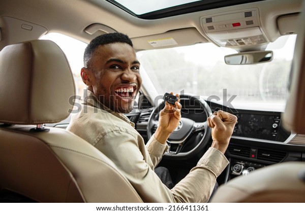 Joyful african american guy holding auto key\
shaking fists sitting in automobile\
