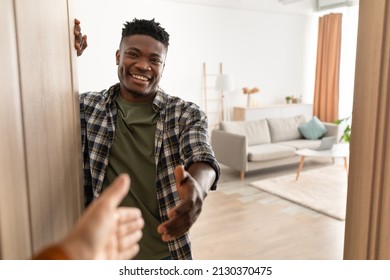 Joyful African American Guy Stretching Hand For Handshake With Somebody Standing Near Opened Door Of His Home, Smiling To Camera. Real Estate Ownership And Purchase. Welcome To My House Concept