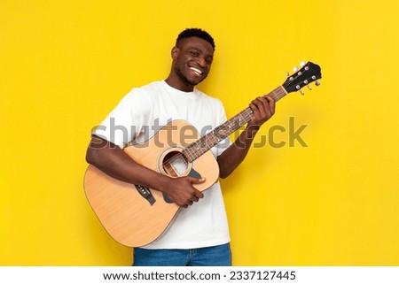 joyful african american man holds acoustic guitar and sings on yellow isolated background, the guy the artist plays musical instrument
