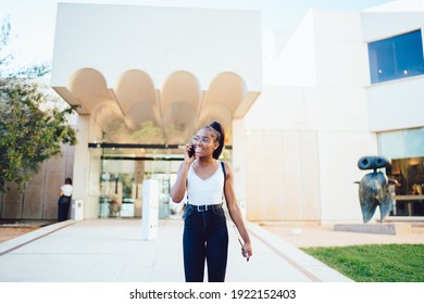 Joyful African American Student Leaving School Building Using Mobile Application For Discussing Positive Communication, Toothy Hipster Girl In Classic Spectacles Laughing While Talking In Roaming