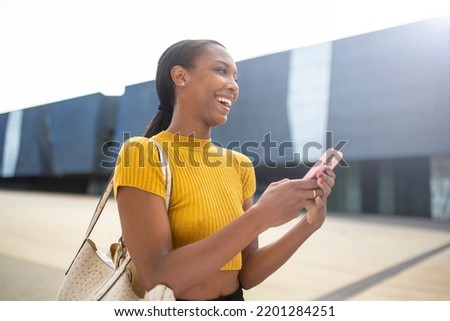 Joyful african american woman laughing while using smart phone outdoors in city