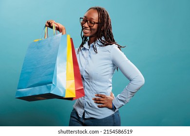 Joyful african american young adult person holding mall purchases and enjoying goods. Happy excited woman smiling at camera after shopping spree at mall while holding retail store bags